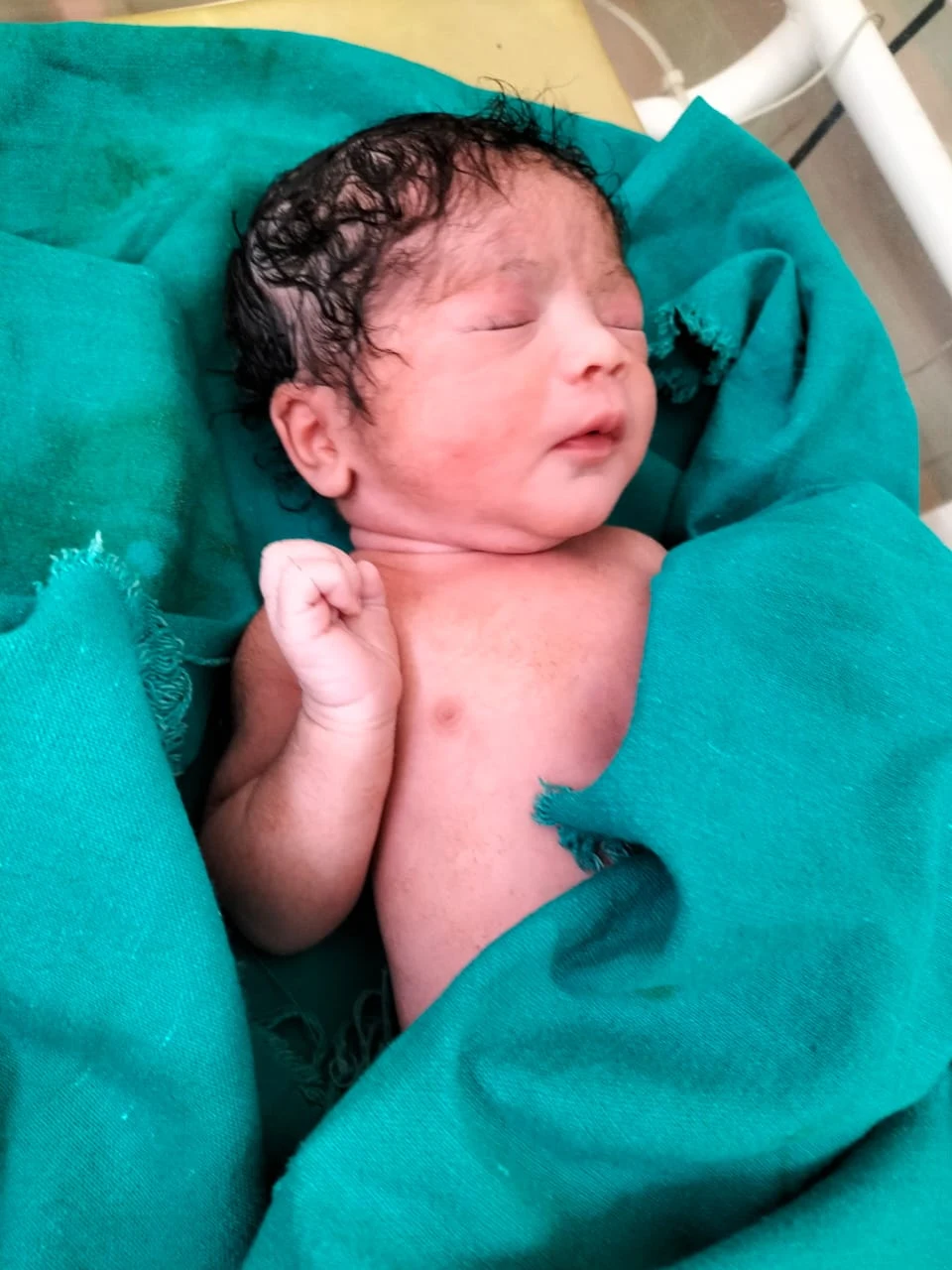 A newborn baby wrapped in a green cloth after delivery